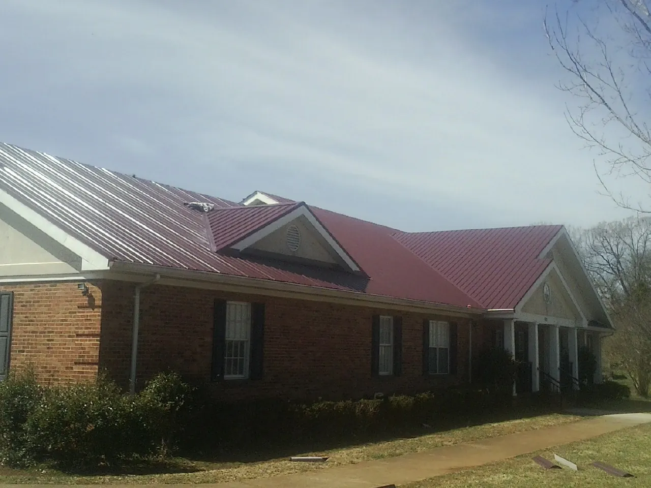 Red metal roof with gabled entries on a long brick building, from a Hail Damage Roof Repair job in Apalachicola