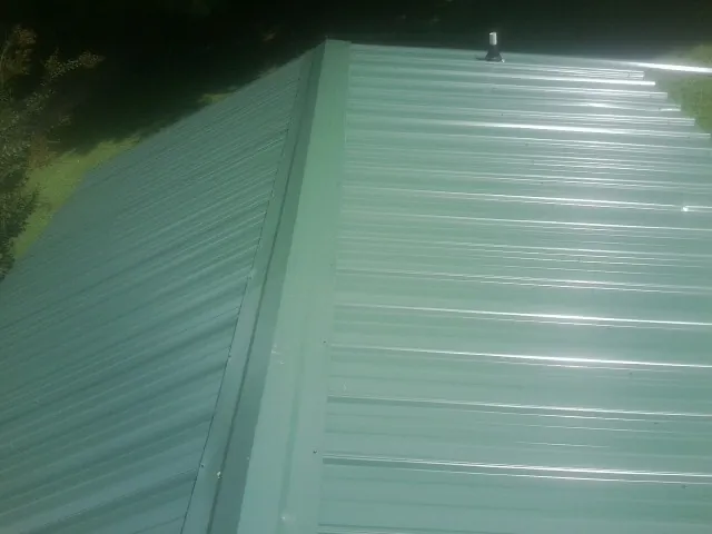 New green metal panels meeting at the ridge of a roof — Flat Roof Repair work by our crew in Apalachicola