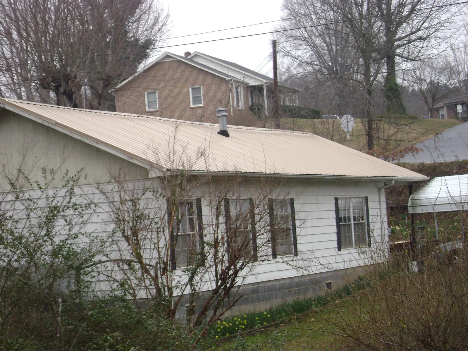Tan metal roof on a white sided house set into a hillside — Commercial Roofing by Roofing Brothers in Apalachicola